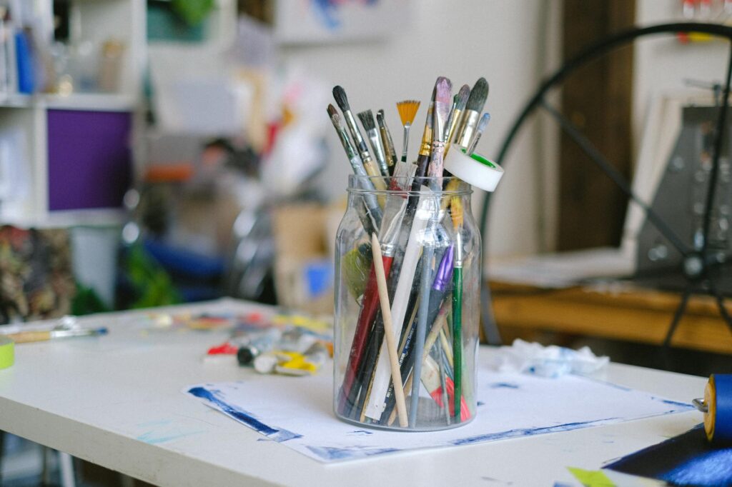 Glass jar with paintbrushes on desk with paint tubes in professional art workshop