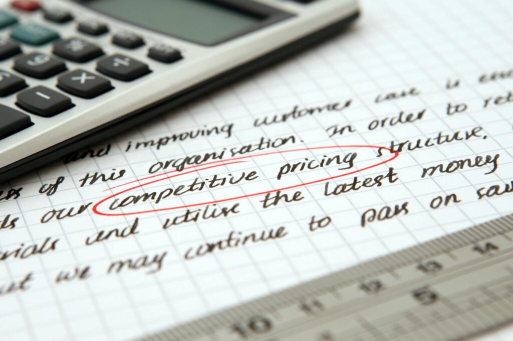 Close-up of handwritten text on graph paper with the phrase "competitive pricing" circled in red, next to a calculator and ruler.